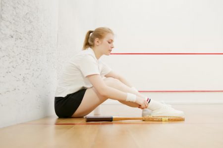 Side view of a young woman resting on a squash court, wearing sportswear and sitting with a racket.