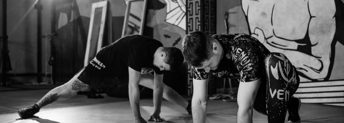 Two men stretching inside a gym, preparing for MMA training in a grayscale setting.